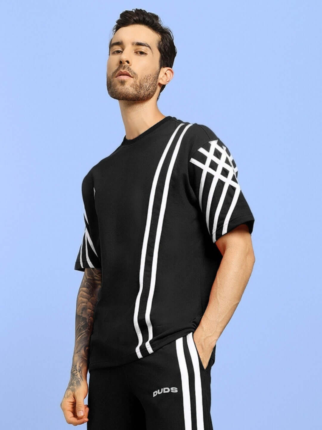 A man wearing a black oversized T-shirt with white stripes, made from premium cotton and elastane, standing against a blue background.