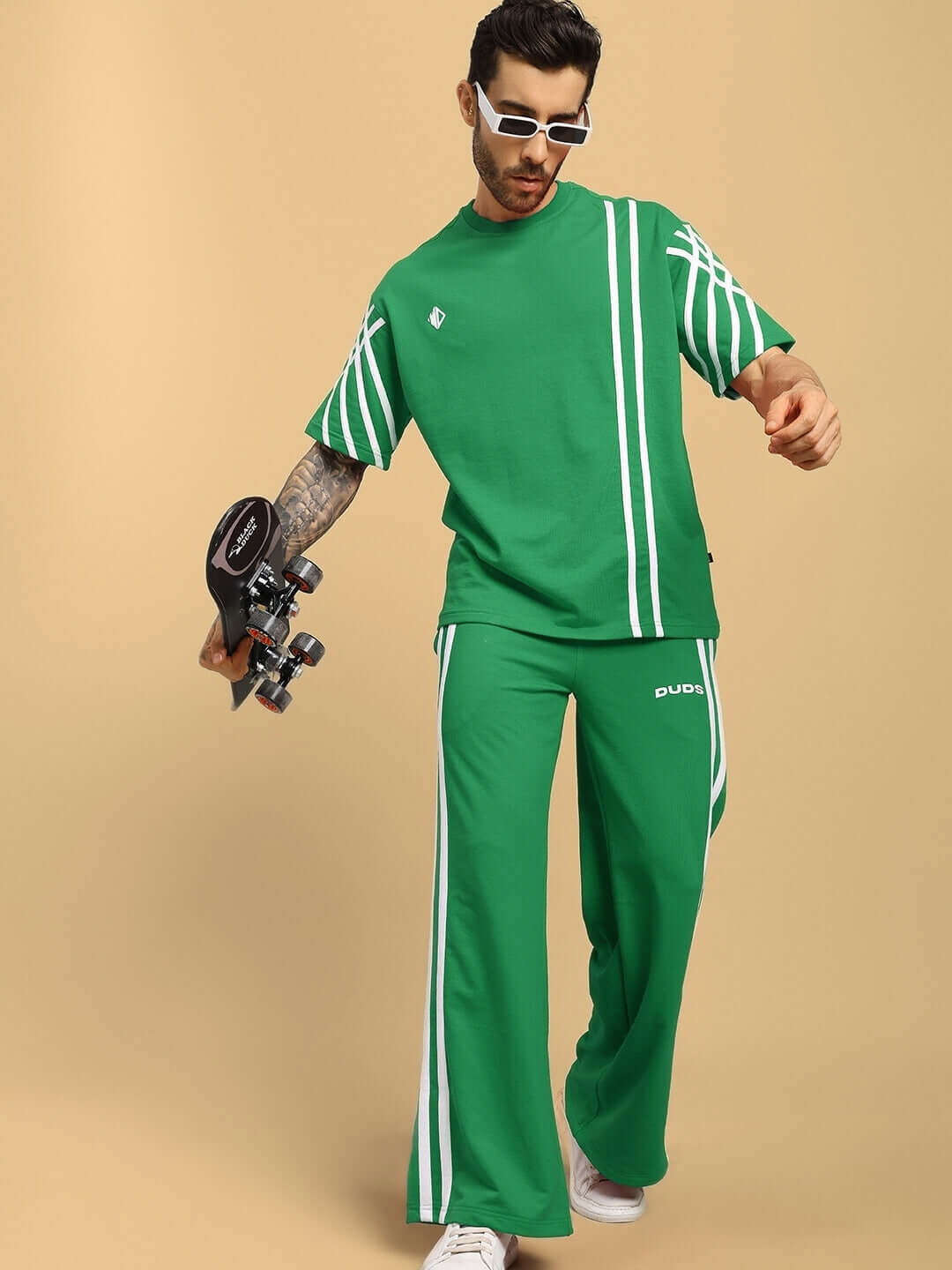 Man wearing a green, oversized striped t-shirt made from premium cotton fabric, holding roller skates, stylish casual outfit.