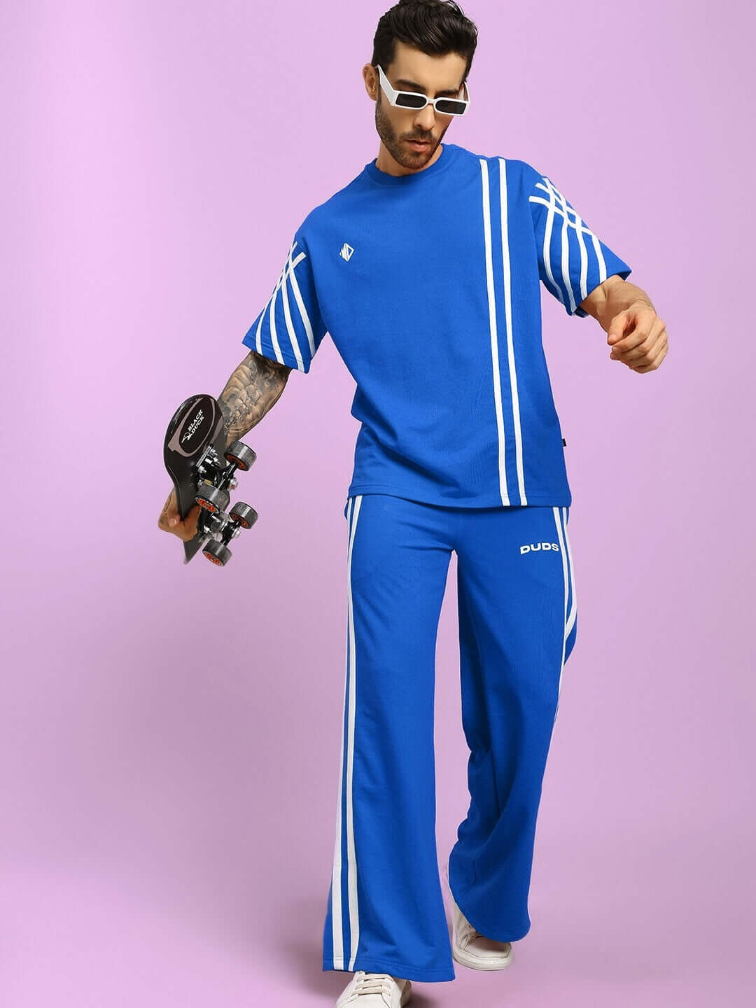 Man wearing blue oversize t-shirt with stripes, holding a skateboard, styled with matching pants; premium cotton fabric.