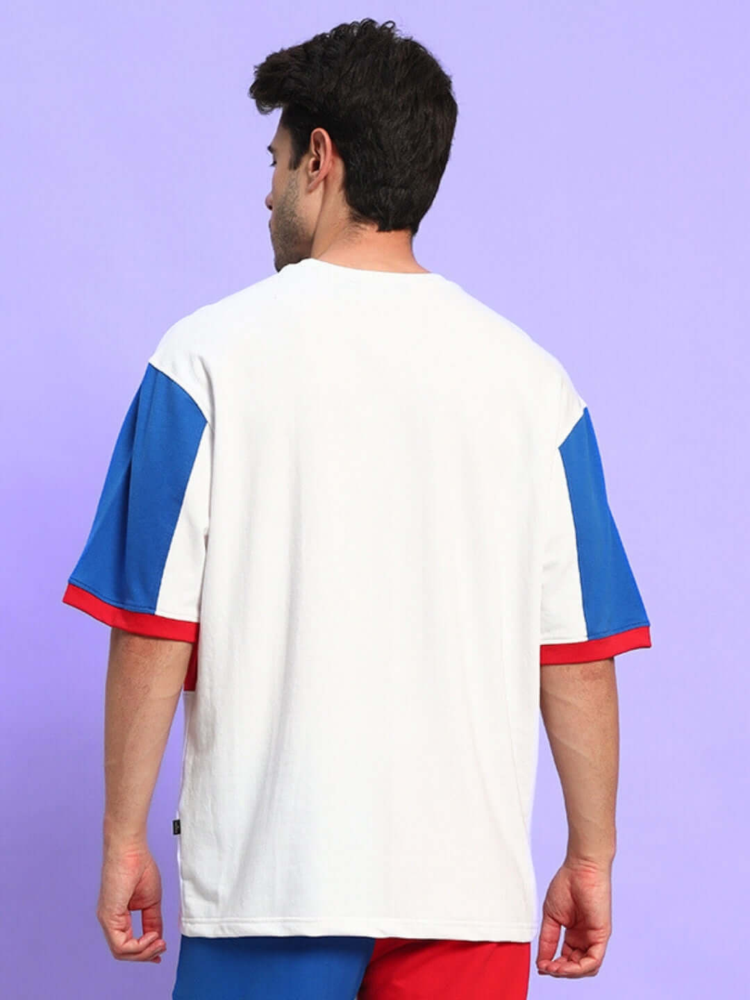 Back view of man wearing URBAN DRIFT OVER-SIZED T-SHIRT MULTI in blue, red, and white colors against a purple background.
