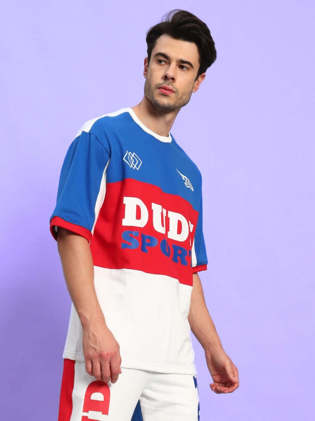 Man wearing URBAN DRIFT OVER-SIZED T-SHIRT MULTI in bold streetwear style against a purple background.