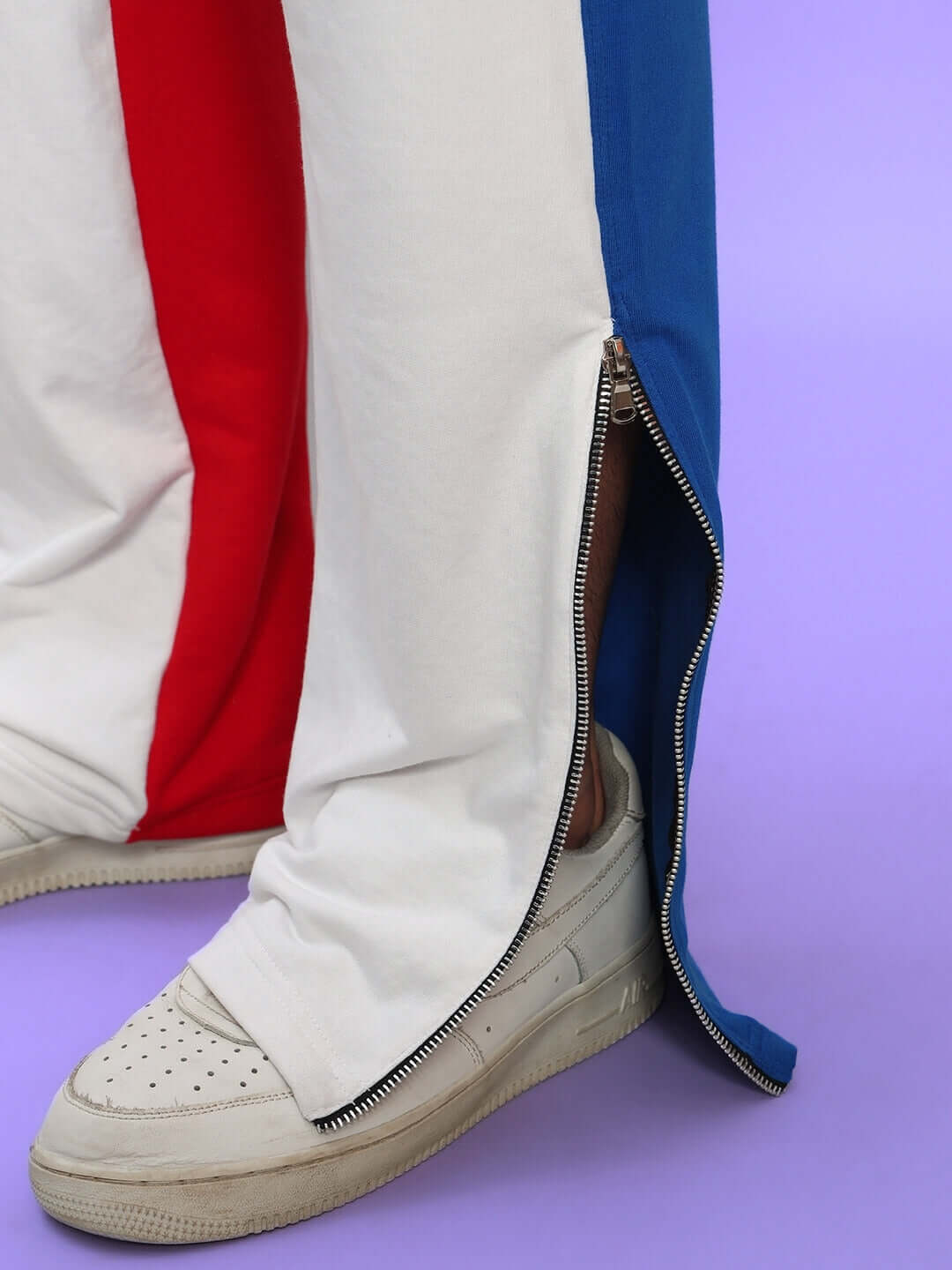 Close-up of URBAN DRIFT Relaxed Fit Joggers in white multi-color with zipper detail, paired with white sneakers, on a purple background.
