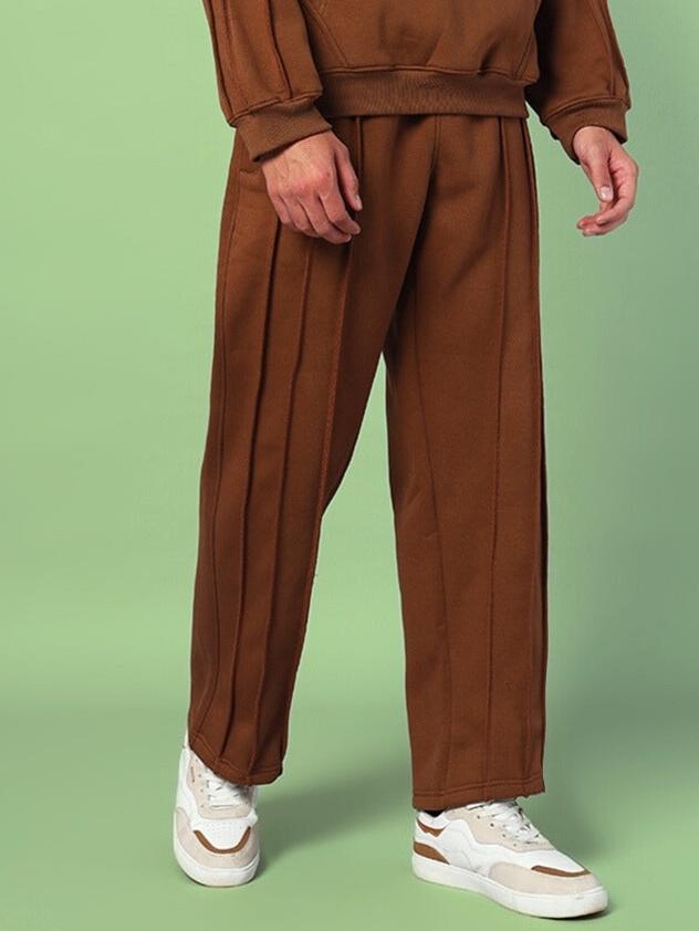 Man wearing URBAN FLEECE CARGO PANTS BROWN with white sneakers against a green background, showcasing relaxed fit and cozy fleece fabric.