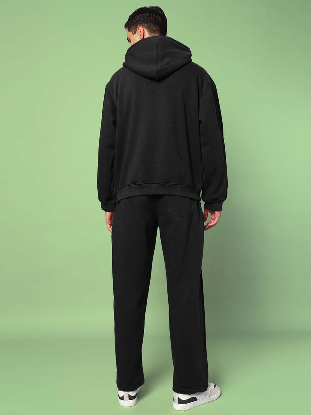 Back view of person wearing URBAN SOLID PLATED FLEECE CO-ORD BLACK, showcasing the hoodie and joggers in solid black with plated detailing.
