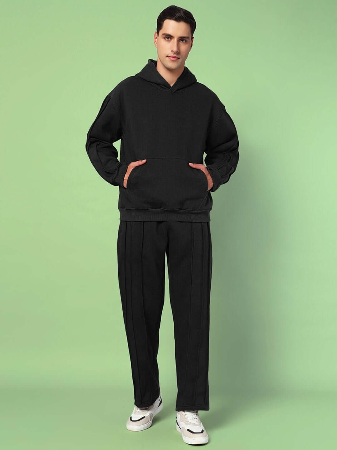 Man wearing the URBAN SOLID PLATED FLEECE CO-ORD BLACK with hoodie and joggers against green background.
