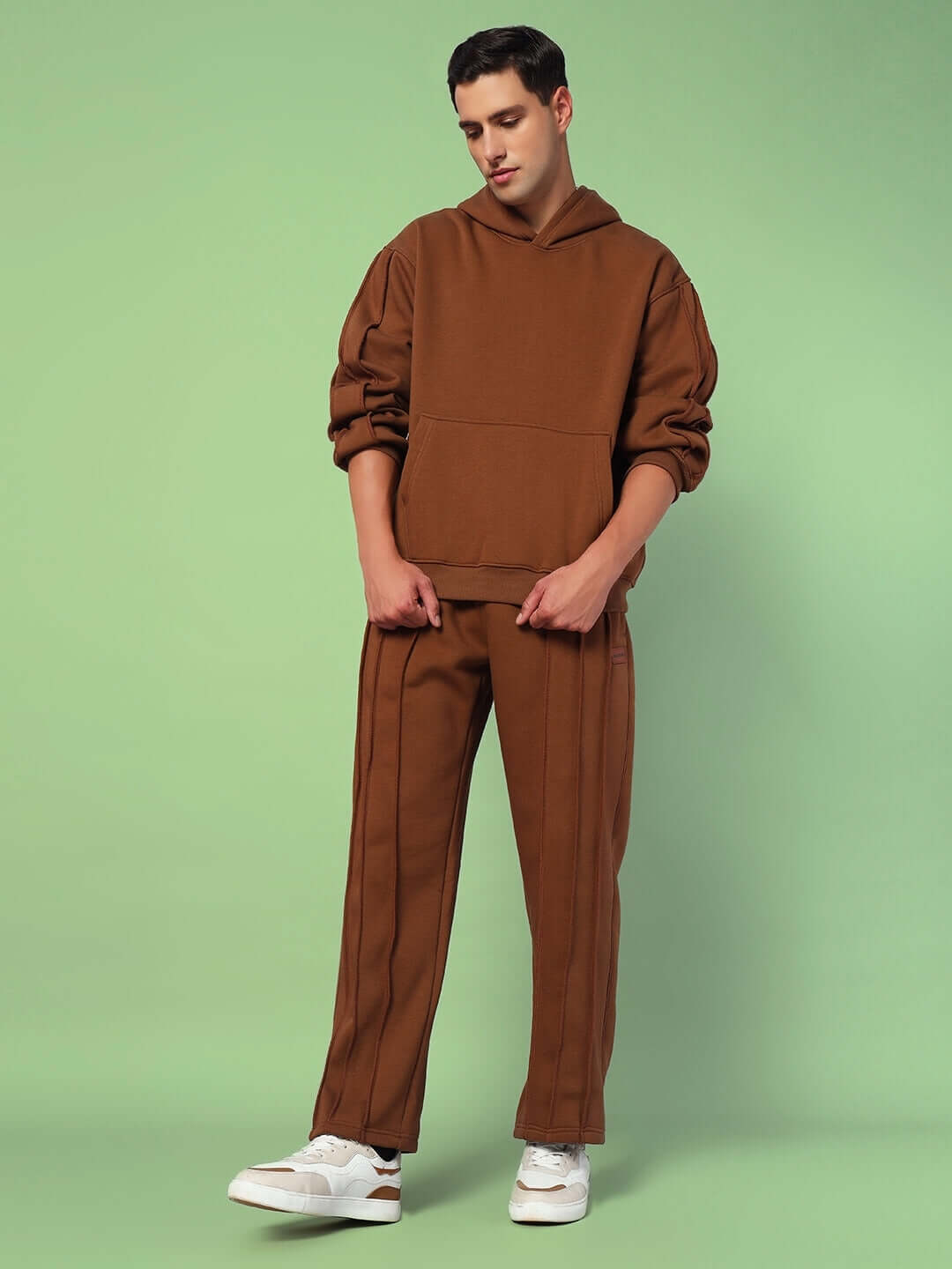 Model wearing Urban Solid Plated Fleece Hoodie Brown, showcasing relaxed fit and modern design against a green background.