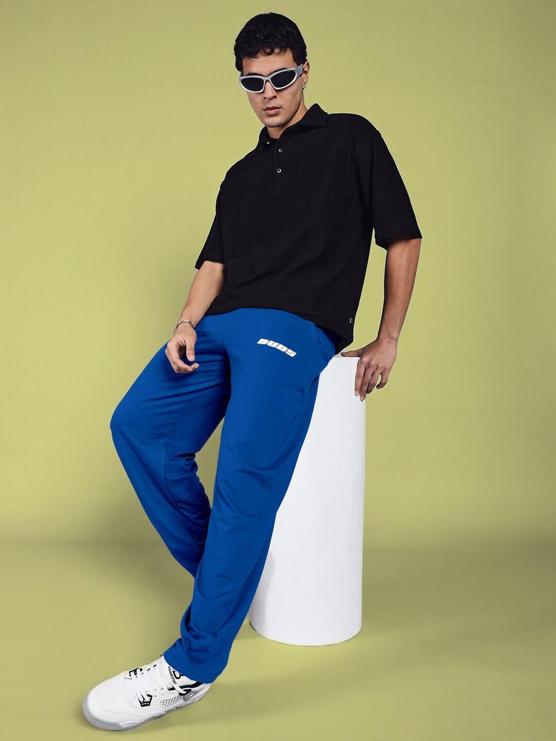 Model wearing blue relaxed-fit joggers from DUDS, paired with black polo and sneakers, posing with casual confidence.