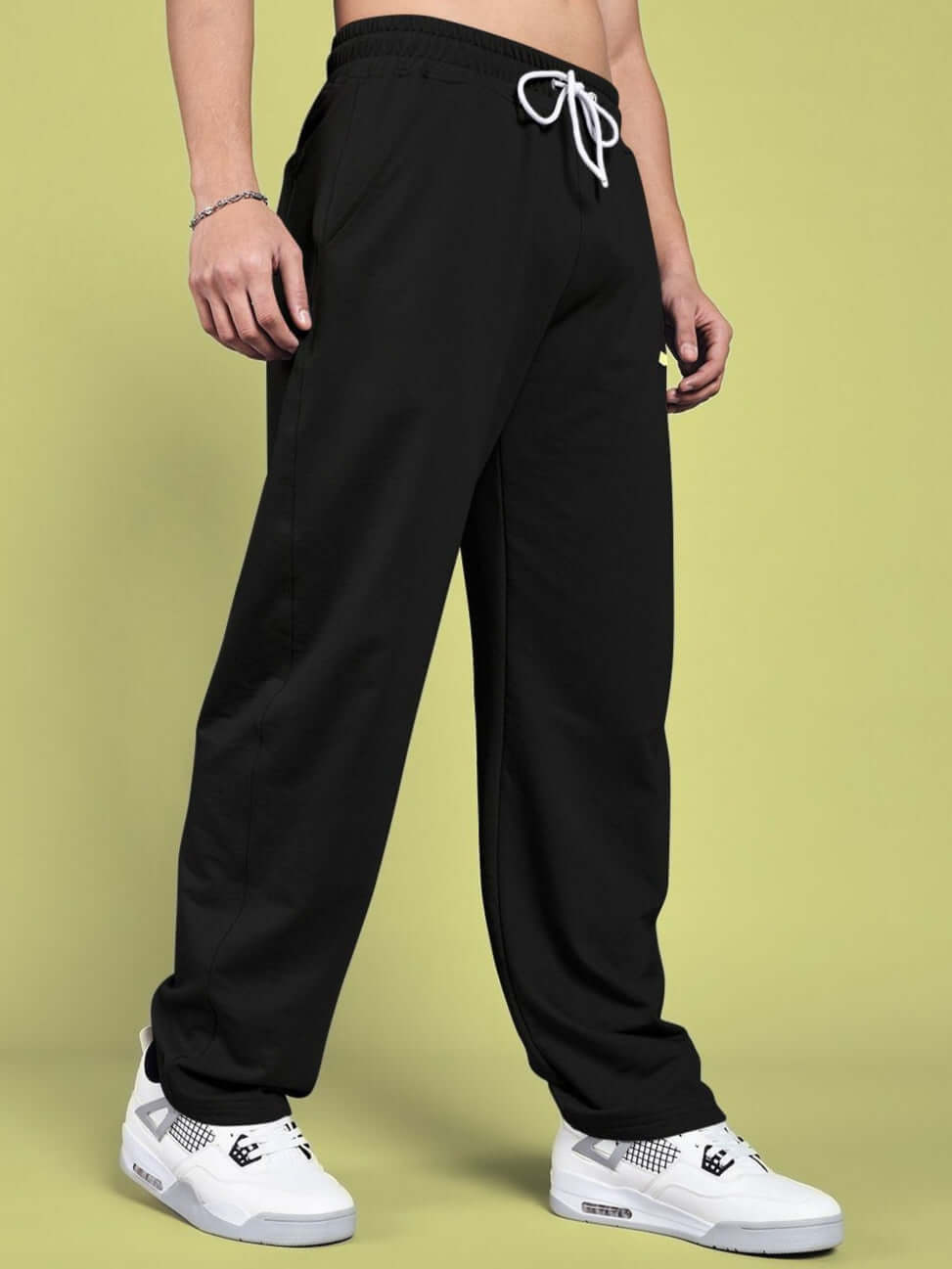 Person wearing black relaxed-fit joggers with white sneakers standing against a green background.