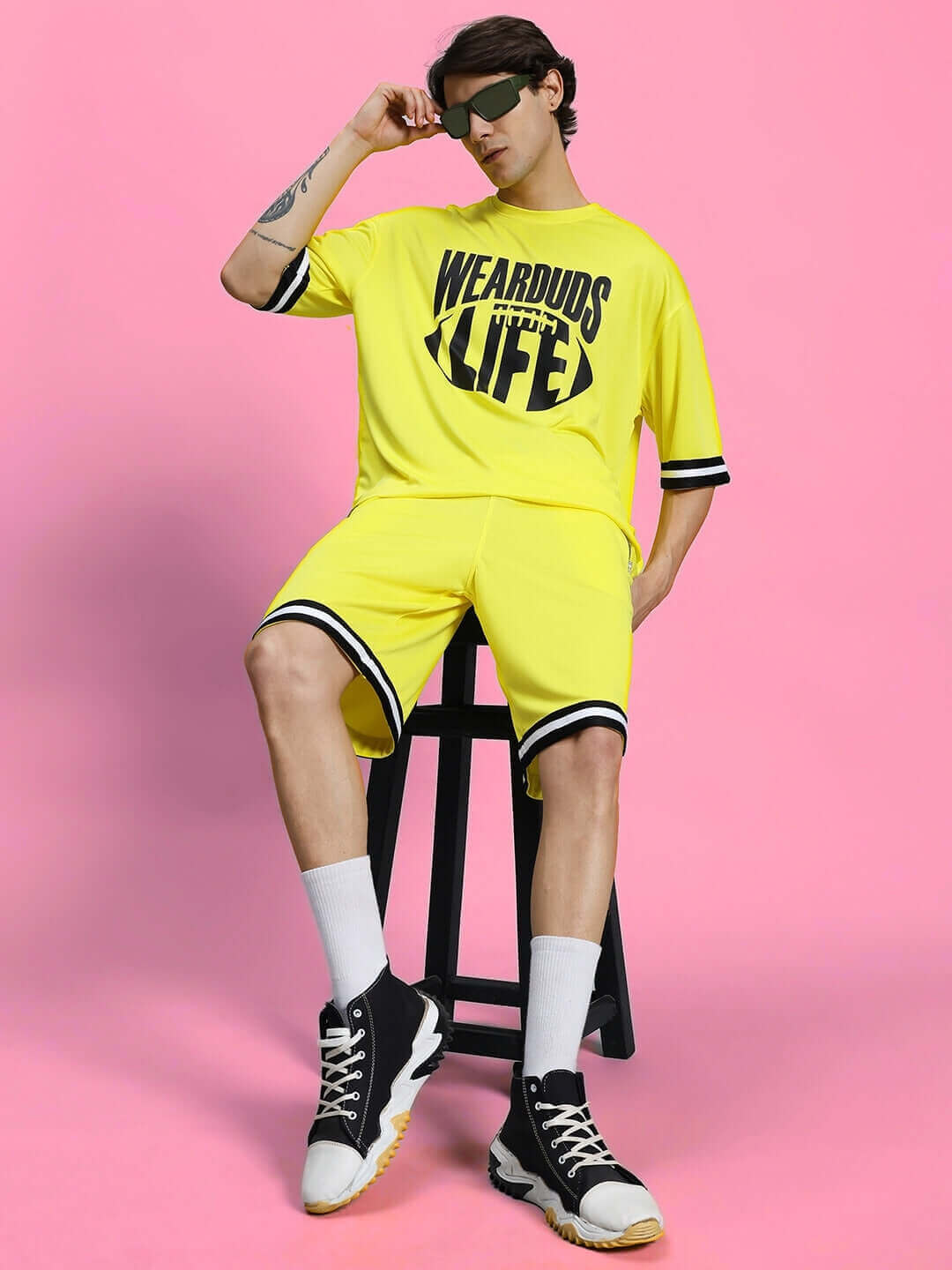 Man wearing yellow VIGOR REGULAR FIT SHORTS paired with matching shirt against pink background, sporty and stylish look.