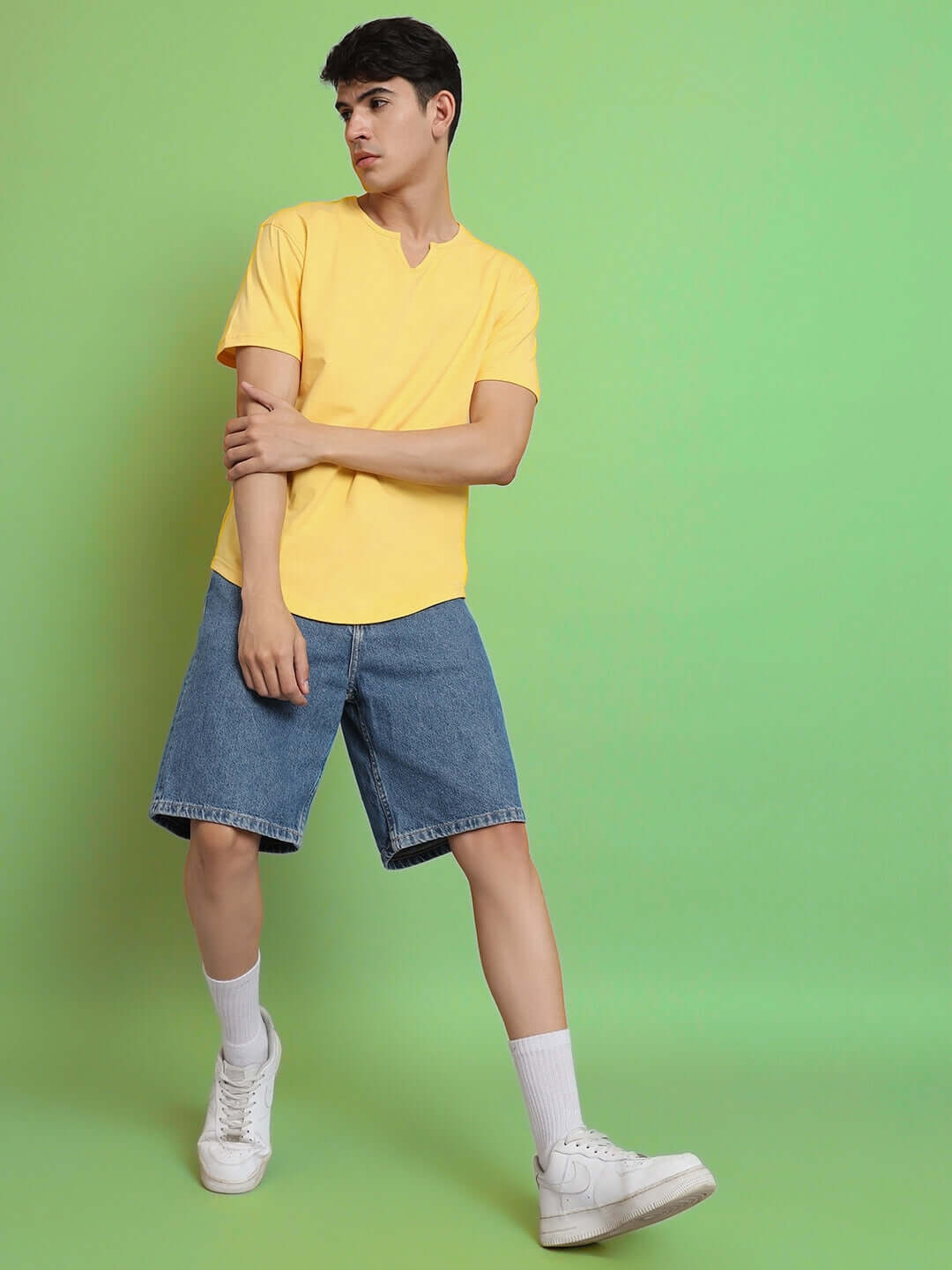 Model wearing VIKING Regular Fit Yellow T-Shirt, 100% cotton, perfect for casual wear, shown with denim shorts, green background.