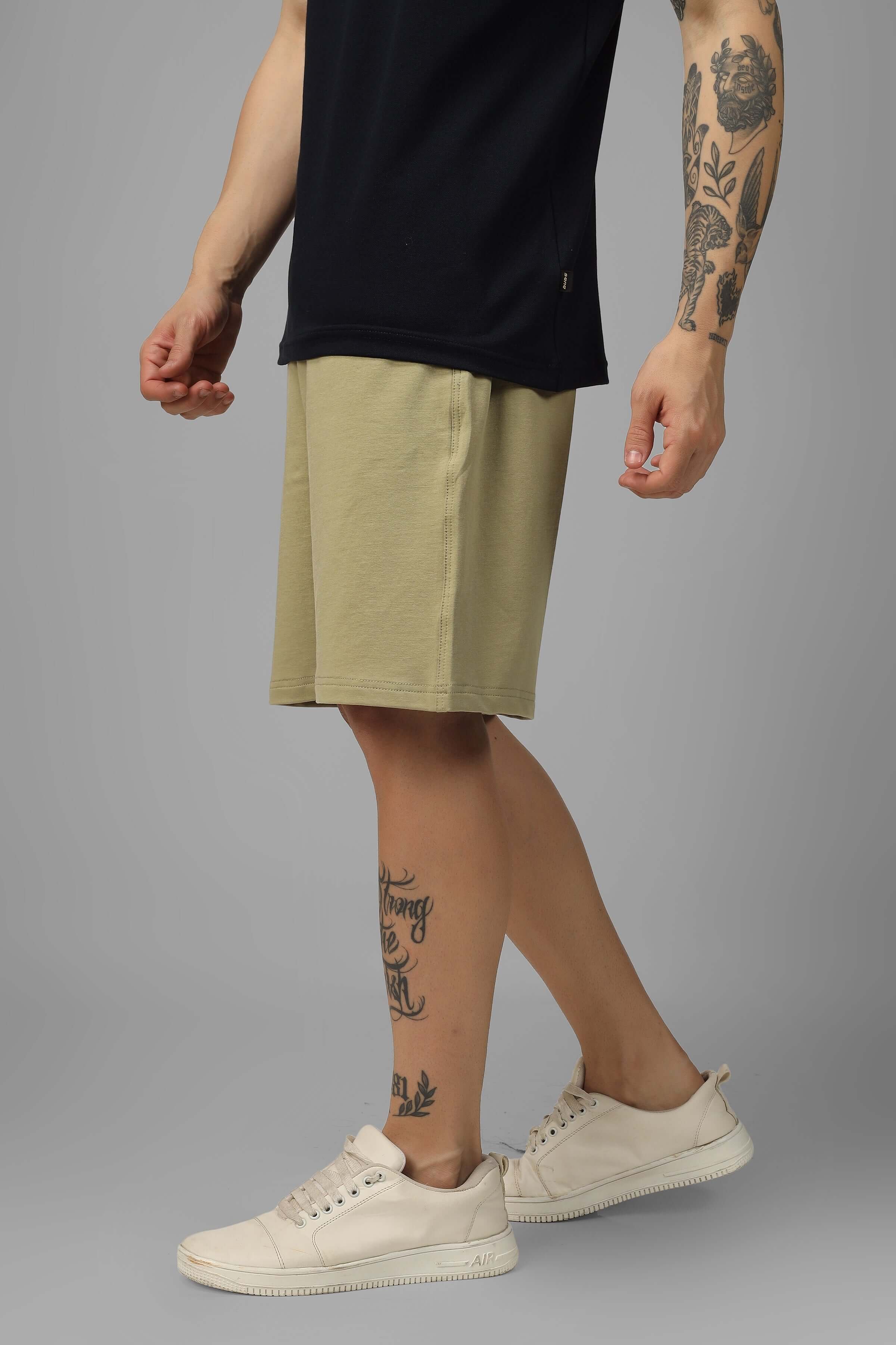 Model wearing Vintage Regular Fit Shorts in Gravel Green, showcasing casual style with sneakers and tattoos.