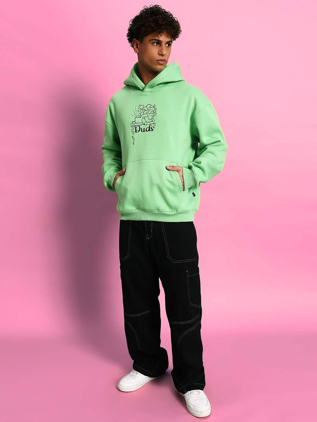 Model wearing VOODO OVERSIZED FLEECE HOODIE GREEN against pink background.