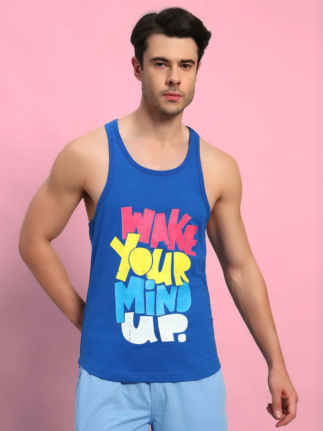 Man wearing WAKE UP GYM T-SHIRT ROYAL BLUE with colorful text on a pink background.