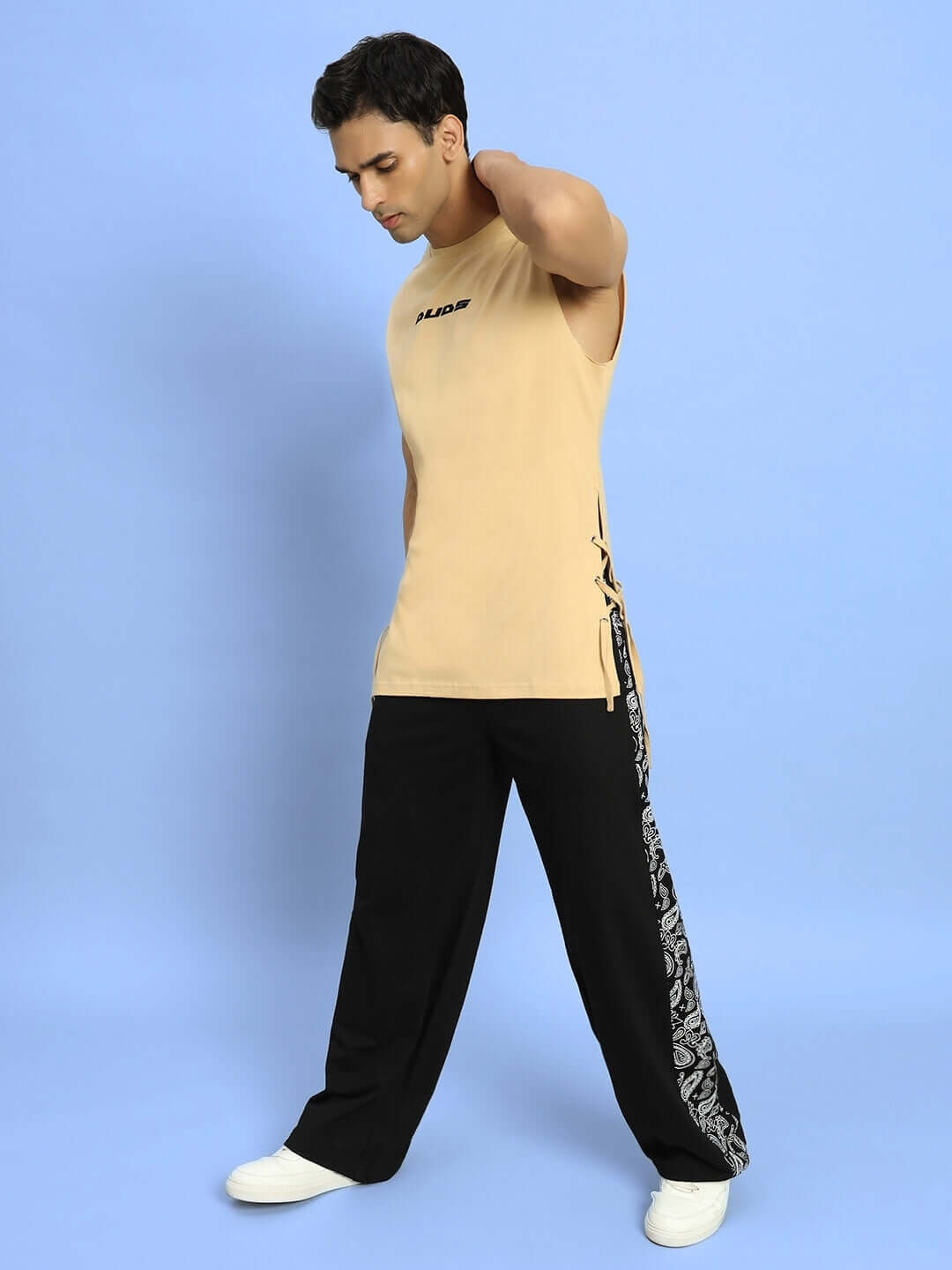 Man wearing WALTZ RELAXED FIT JOGGERS BLACK with a sleeveless beige shirt standing on a light blue background, demonstrating comfort and ease.