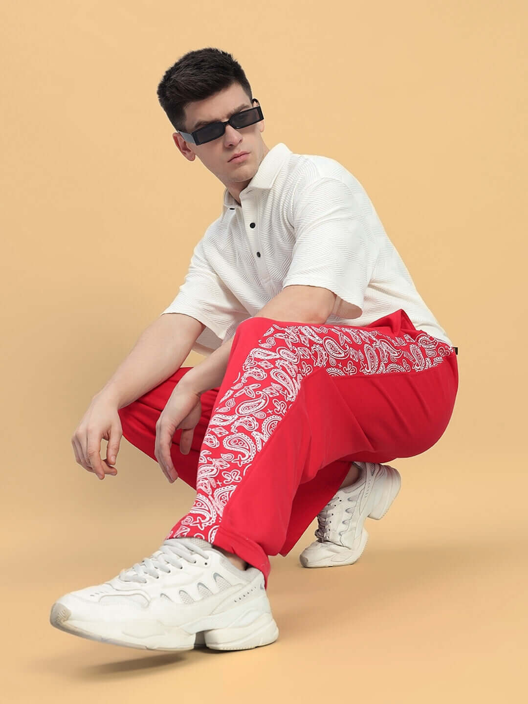 Model wearing Waltz Relaxed Fit Joggers in red with paisley design, styled with white sneakers and polo shirt.
