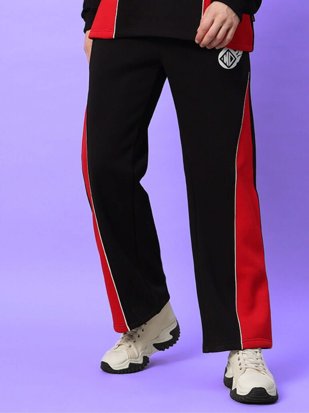 Man wearing WD FIREBALL COLORBLOCK CO-ORD BLACK RED joggers with white sneakers on a purple background.