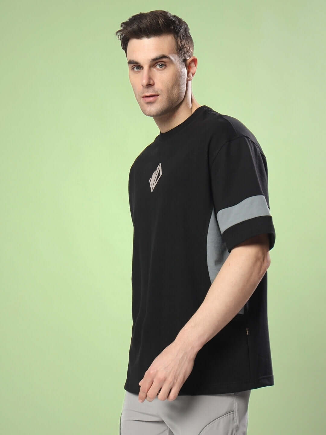 Model wearing WD GORBCORE Oversized T-Shirt in Black-Grey, made from premium heavy-gauge cotton fabric, against a green background.