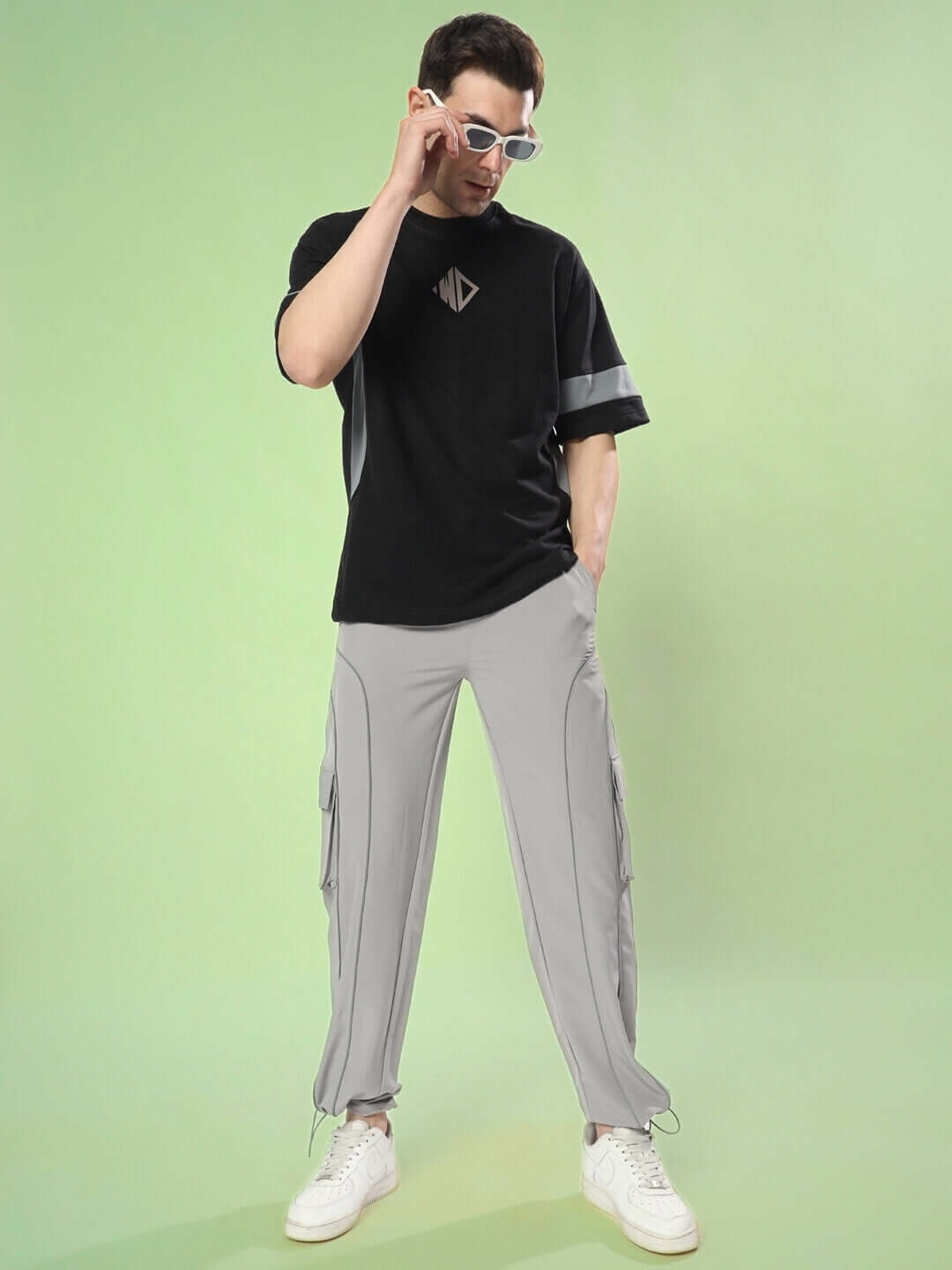 Model wearing WD Gorpcore oversized black-grey T-shirt, premium cotton, French terry fabric, paired with stylish grey pants, against green backdrop.