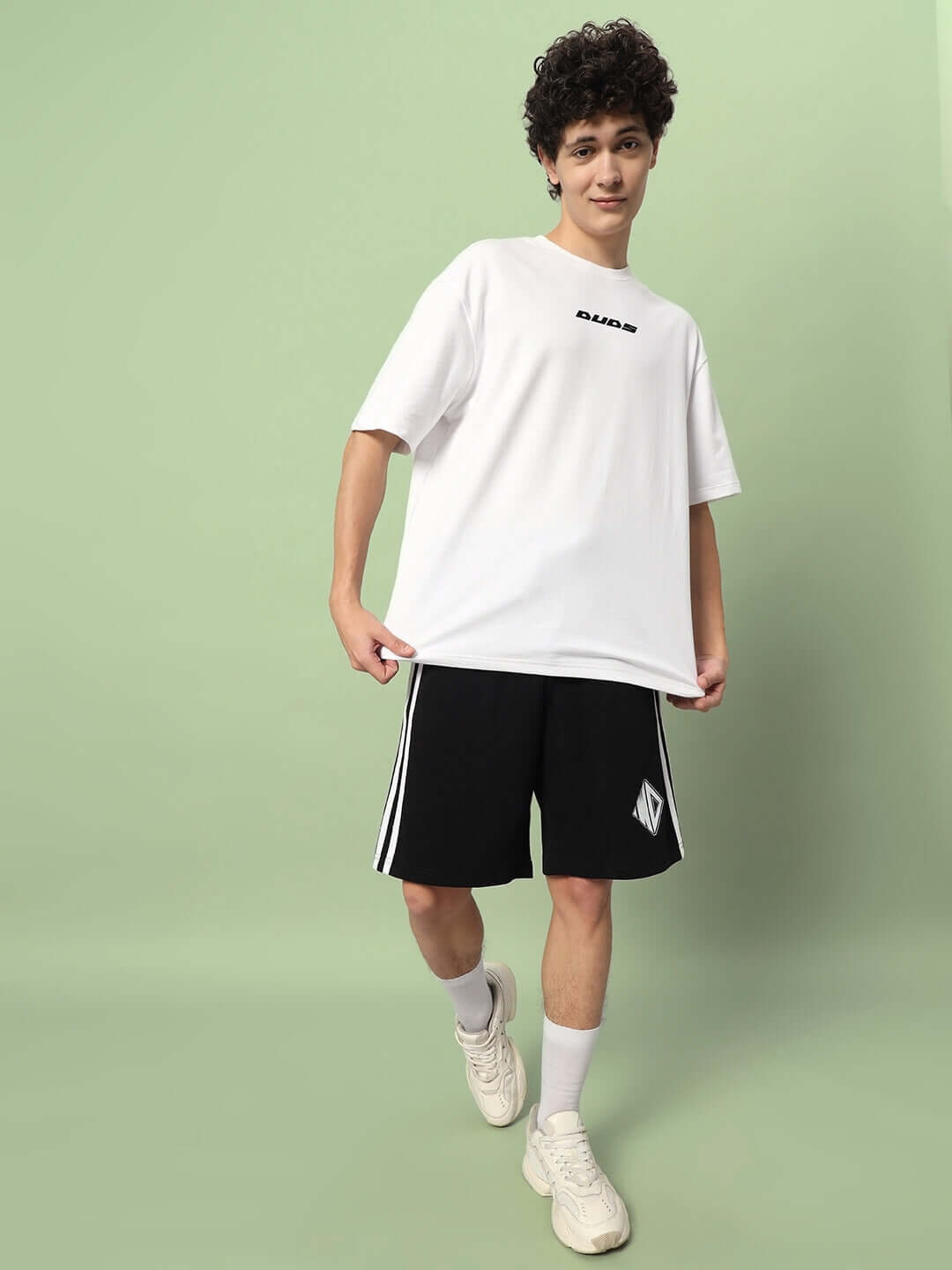 Man wearing DUDS branded white shirt and black shorts standing against a light green background, showcasing WD Premium Regular Fit Shorts.
