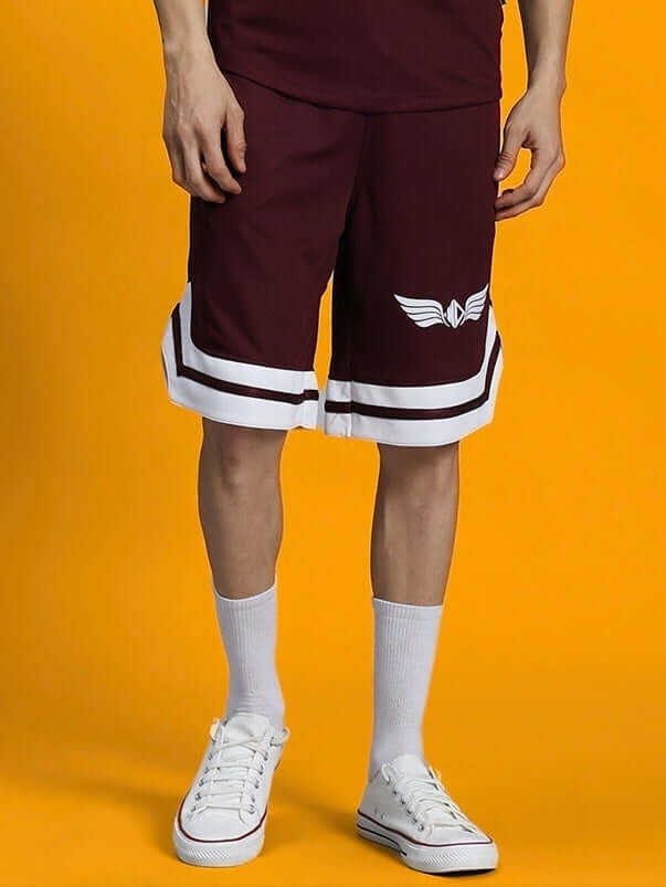 Man wearing WD WINGS REGULAR FIT SHORTS MAROON with white sneakers against a yellow background, showcasing comfort and style.