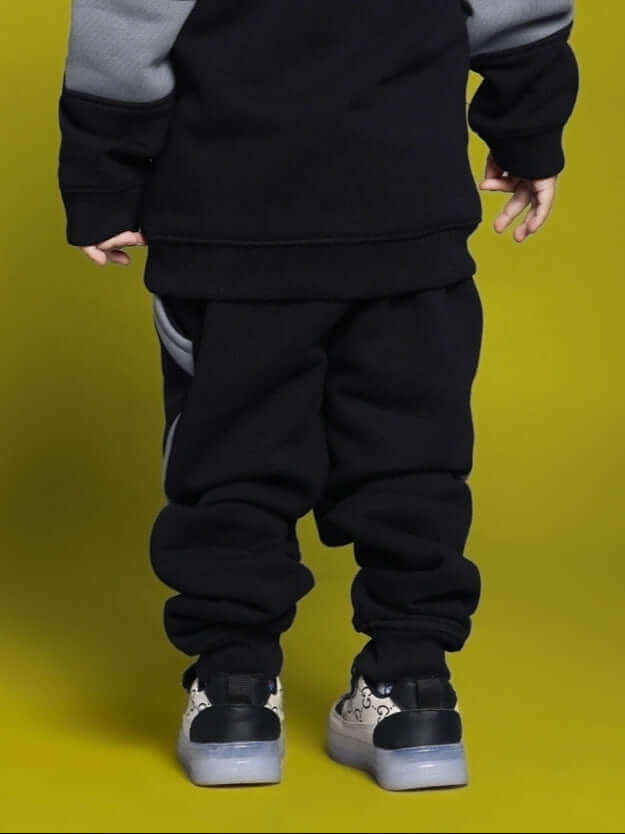 Child wearing black and gray WD Gorbcoure fleece colorblock pants, showcasing back view against yellow background.