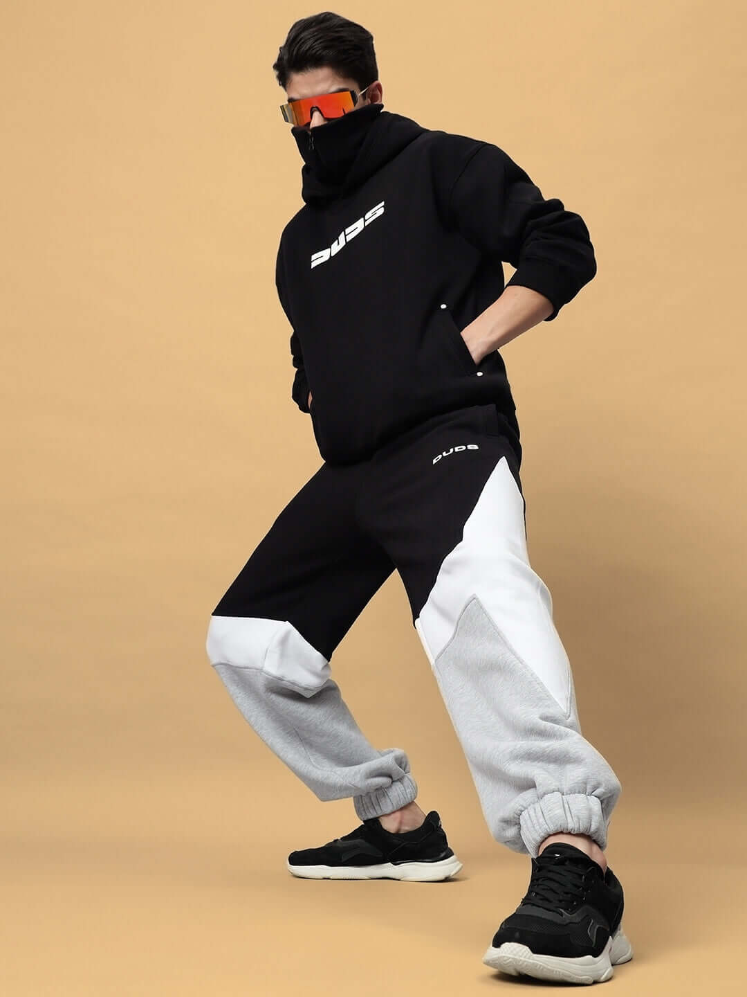 Model wearing WD Sword Fleece Colorblock Cargo Pant with bold colorblock design, black hoodie, and sneakers, posing in style.