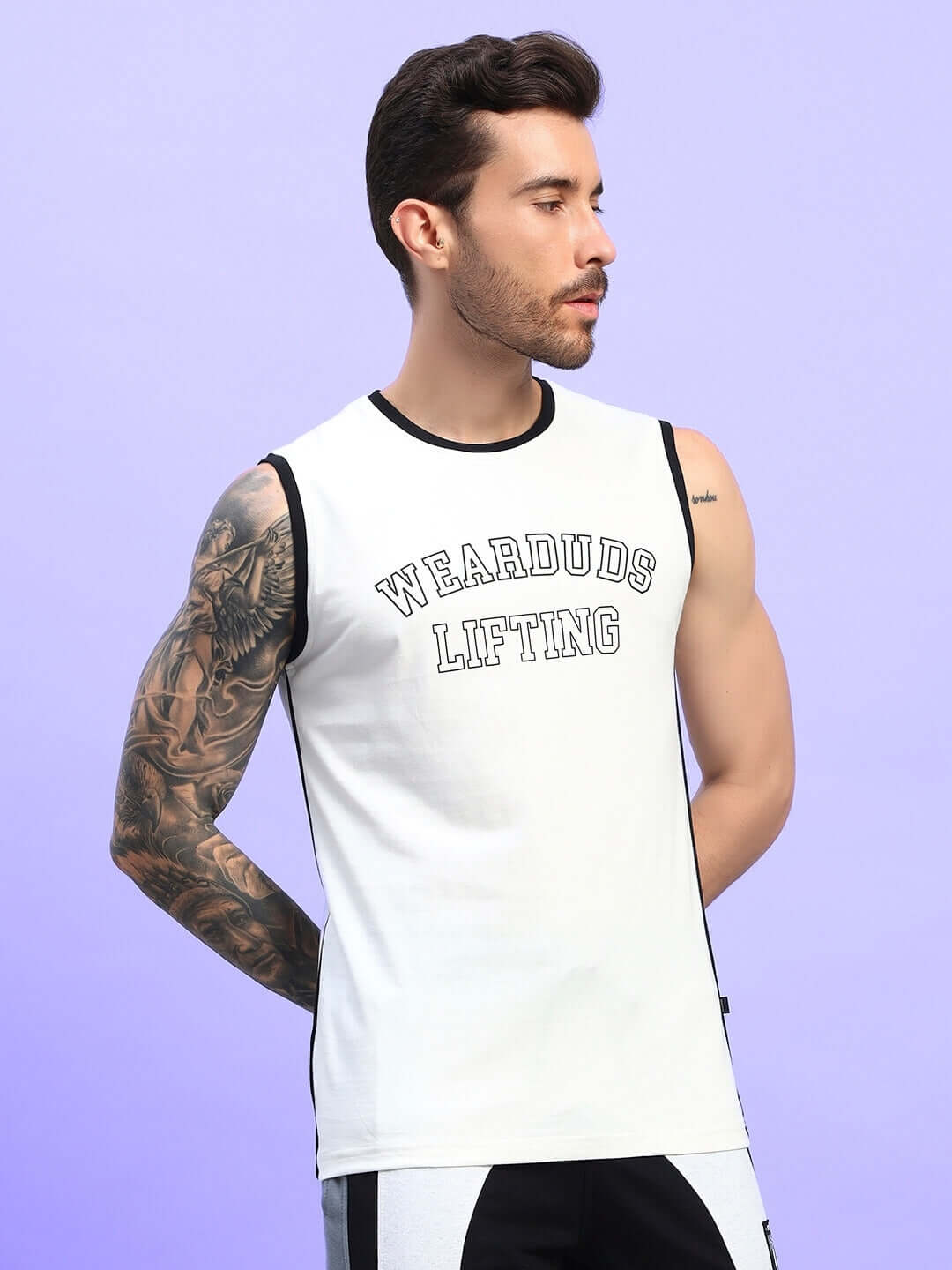 Man wearing a sleeveless white t-shirt with 'Wearduds Lifting' print, featuring tattooed arm detail and styled against a purple background.