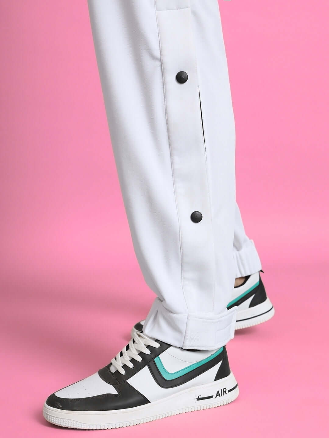 Side view of white hip hop joggers paired with stylish sneakers on a pink background.