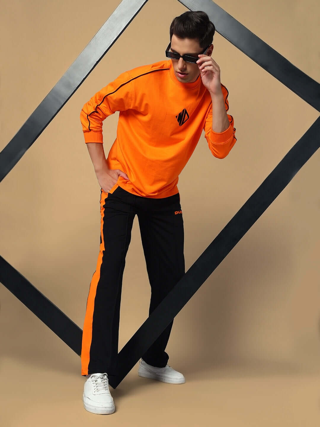 Man wearing WHOPPER OVERSIZED CO-ORD SET ORANGE BLACK, stylish orange top with black pants, showcasing urban fashion in a modern pose.
