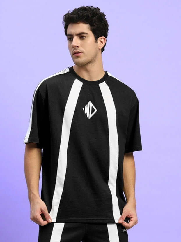 Model wearing WIDELINE OVER-SIZED T-SHIRT BLACK with white stripes on purple background, showcasing relaxed streetwear style.