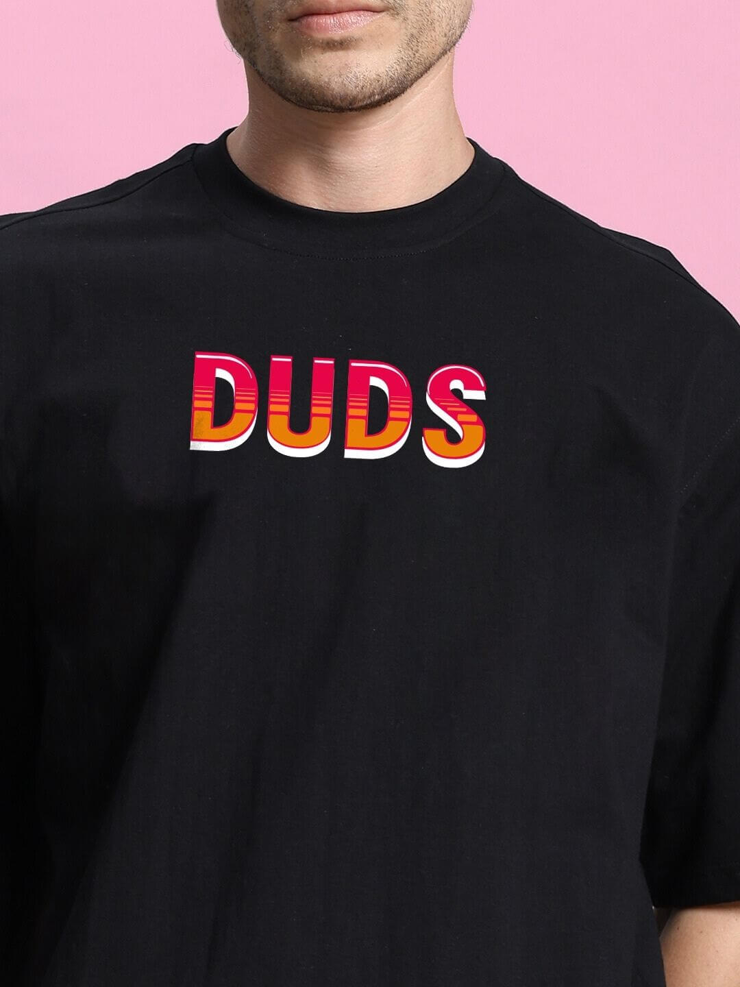 Model wearing the WILD CITY OVERSIZED T-SHIRT BLACK with bold graphic 'DUDS' design against a pink background.