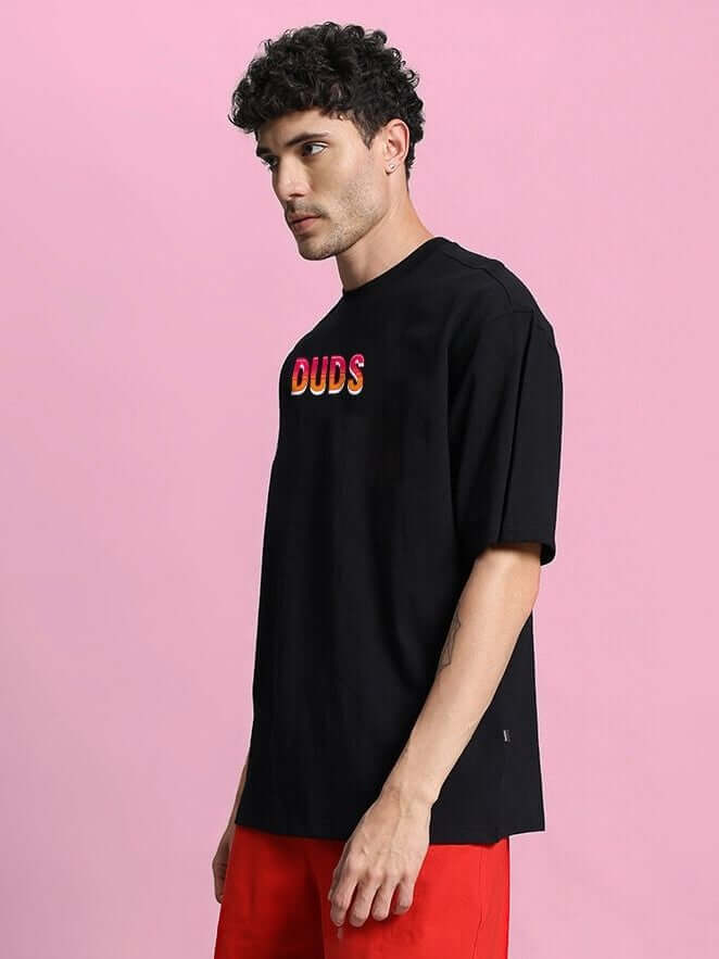 Man wearing WILD CITY OVERSIZED T-SHIRT BLACK with bold graphics against pink background