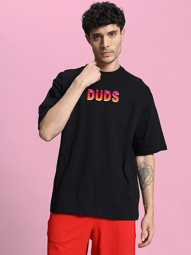 Man wearing WILD CITY OVERSIZED T-SHIRT BLACK with colorful "DUDS" print on pink background.