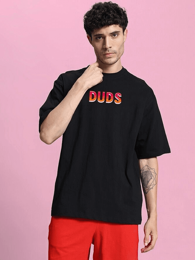 Model wearing WILD CITY OVERSIZED T-SHIRT BLACK with bold graphic, against pink background.