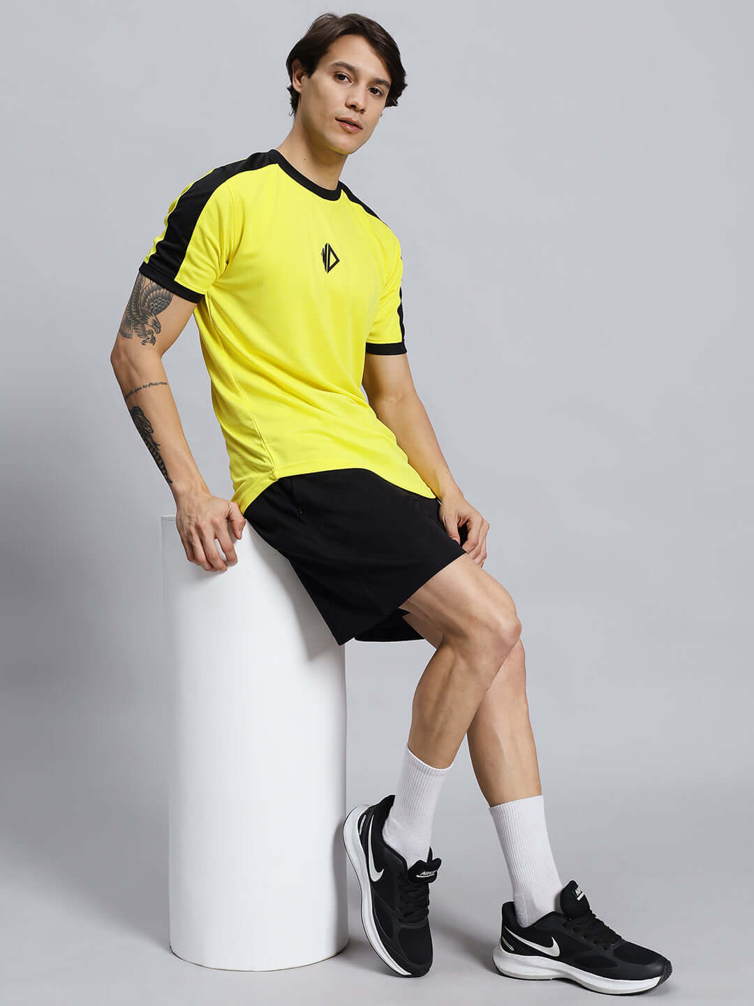 Man wearing WILY TACTICAL REGULAR FIT SHORTS MEN BLACK seated on a cylinder, highlighting style and comfort for outdoor activities.