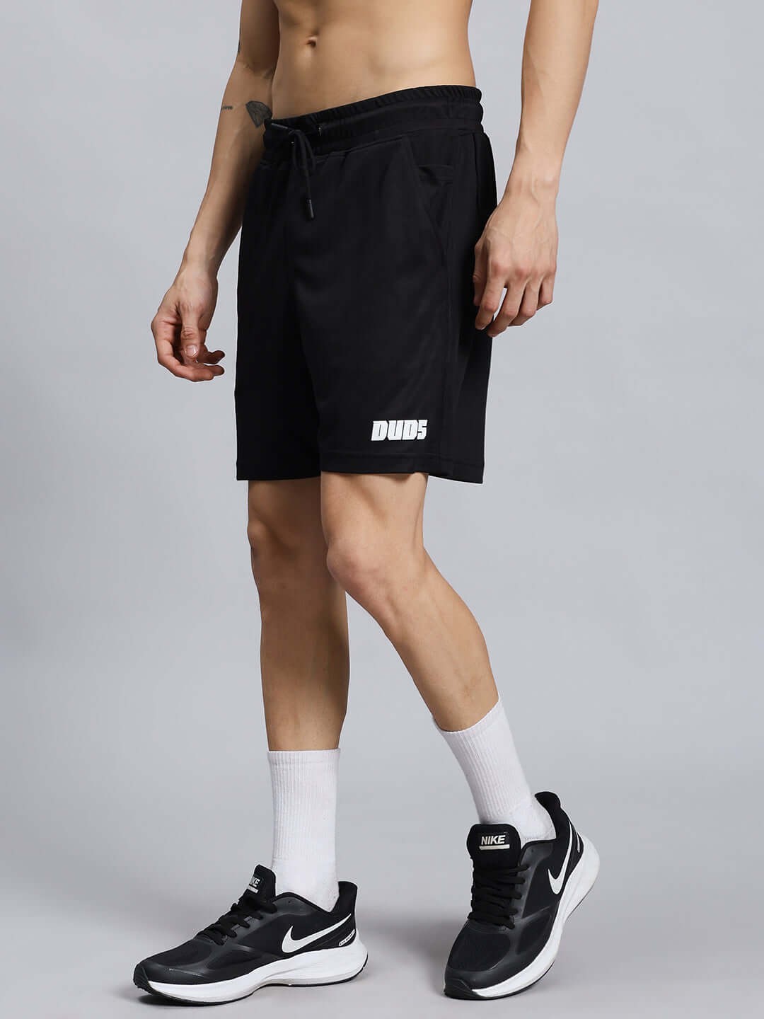 Man wearing WILY TACTICAL REGULAR FIT SHORTS MEN BLACK with sneakers and white socks, showcasing comfort and versatility for outdoor wear.