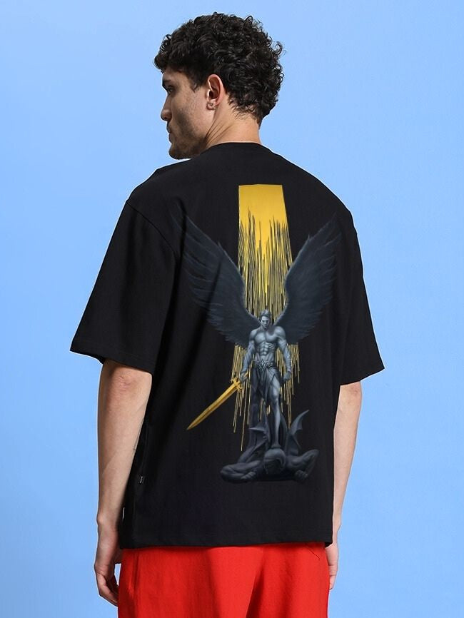 Man wearing WINGED WARRIOR PRINTED OVERSIZED T-SHIRT BLACK featuring a winged warrior graphic against a blue background.