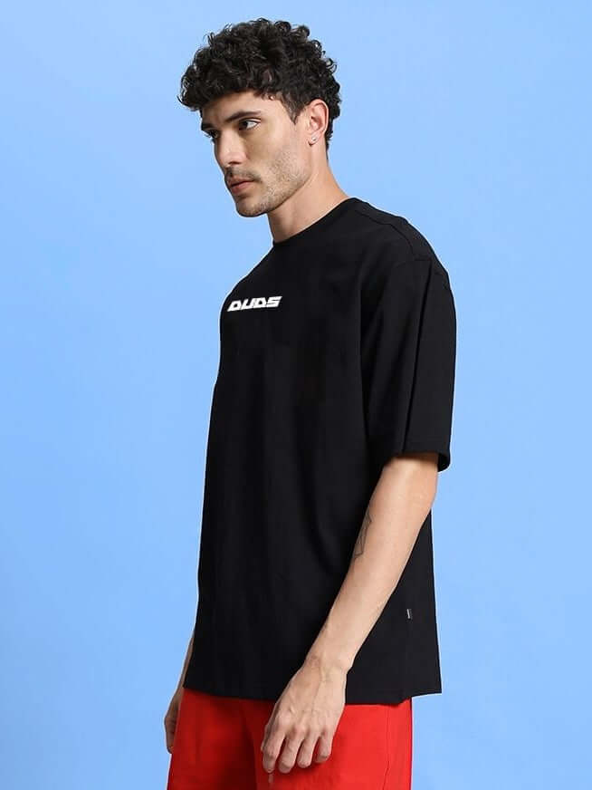 Model wearing WINGED WARRIOR PRINTED OVERSIZED T-SHIRT BLACK against blue background