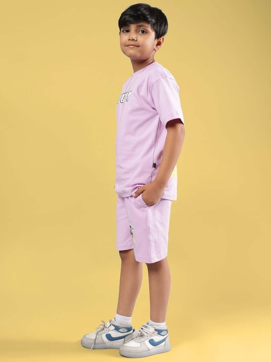 Boy wearing WOLF PACK CO-ORD FOR BOYS & GIRLS LILAC set, featuring shorts and t-shirt, styled with sneakers on a yellow background.