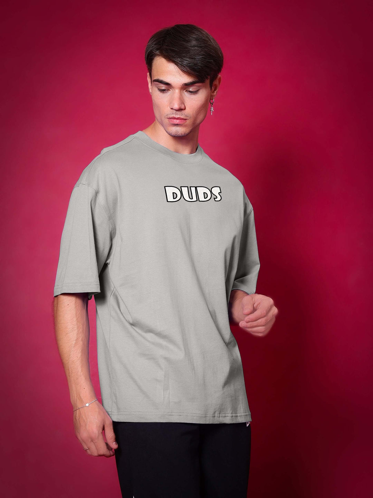 Person wearing WOLF PACK OVER-SIZED T-SHIRT GREY against a red background, showcasing comfortable streetwear look.