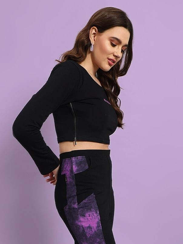 Model wearing black-purple women's viola tie-dye crop top, showcasing side profile with purple details on pants, set against a purple background.