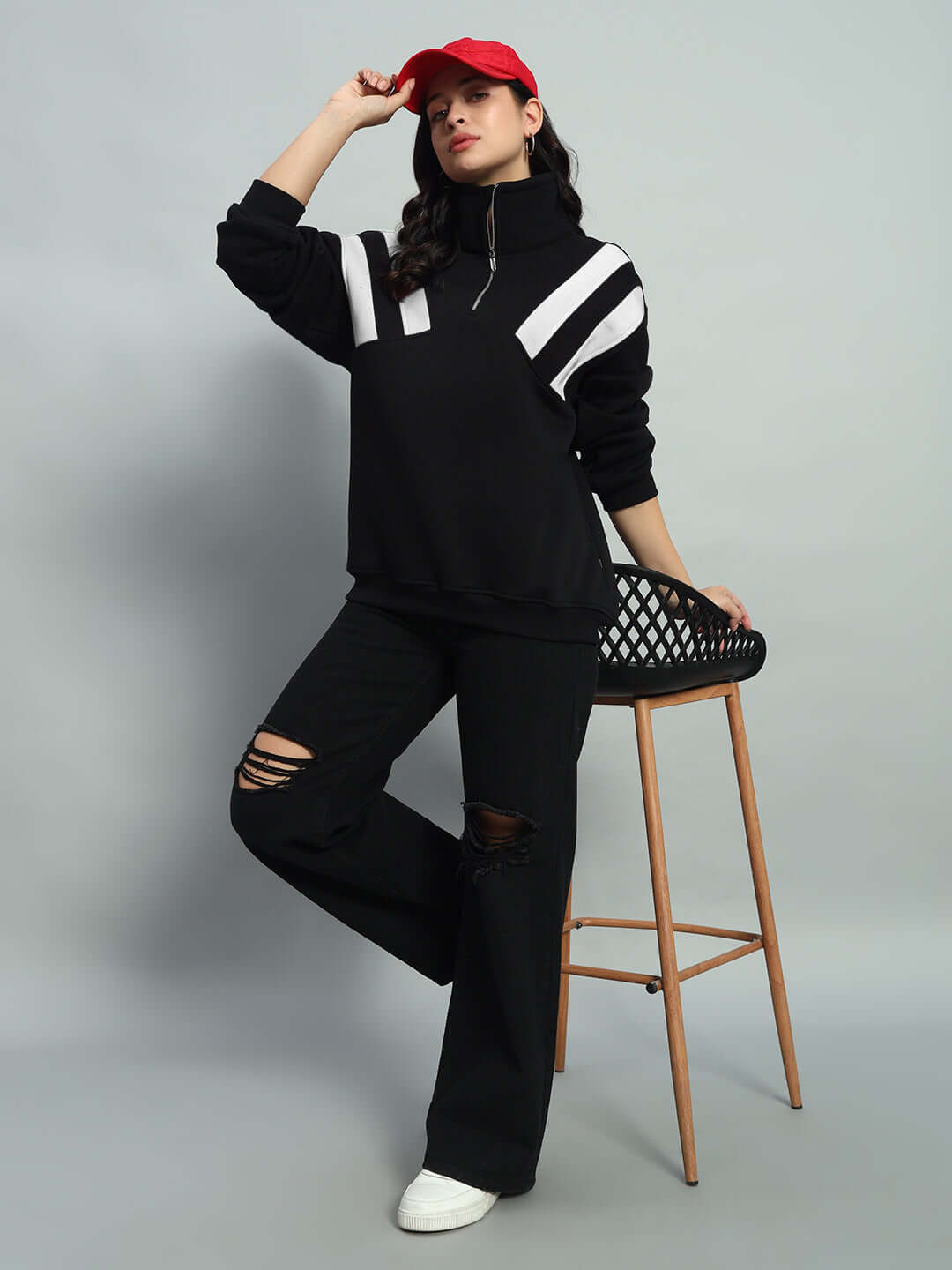 Woman wearing a black-white colorblock fleece jacket with crossbar design, posing stylishly with a red cap indoors.