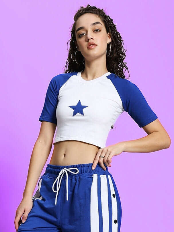 Woman wearing a women's Achorm crop-top in white and blue with a star design, made from premium heavy gauge cotton fabric, standing against a purple background.