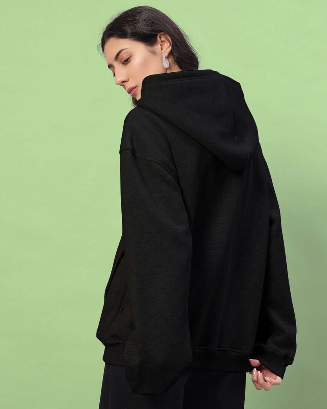 Woman wearing black women's Amarillo fleece hoodie from DUDS, side view with green background. Made to order with custom fit option.