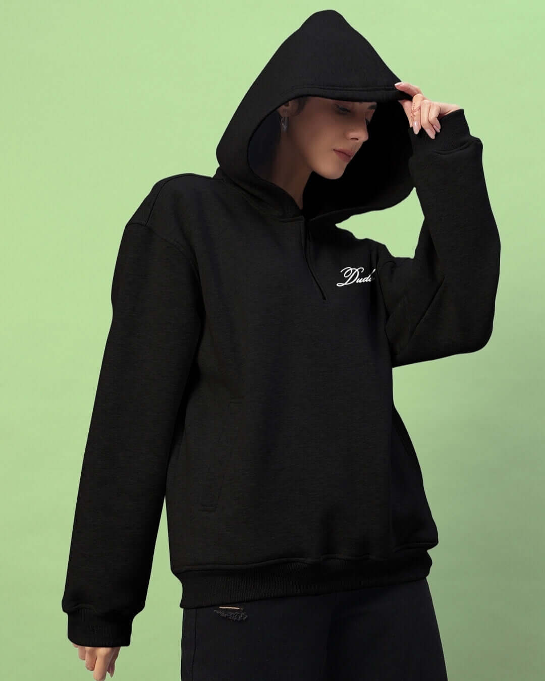 Woman wearing a black Amarillo fleece hoodie with hood up against green background.