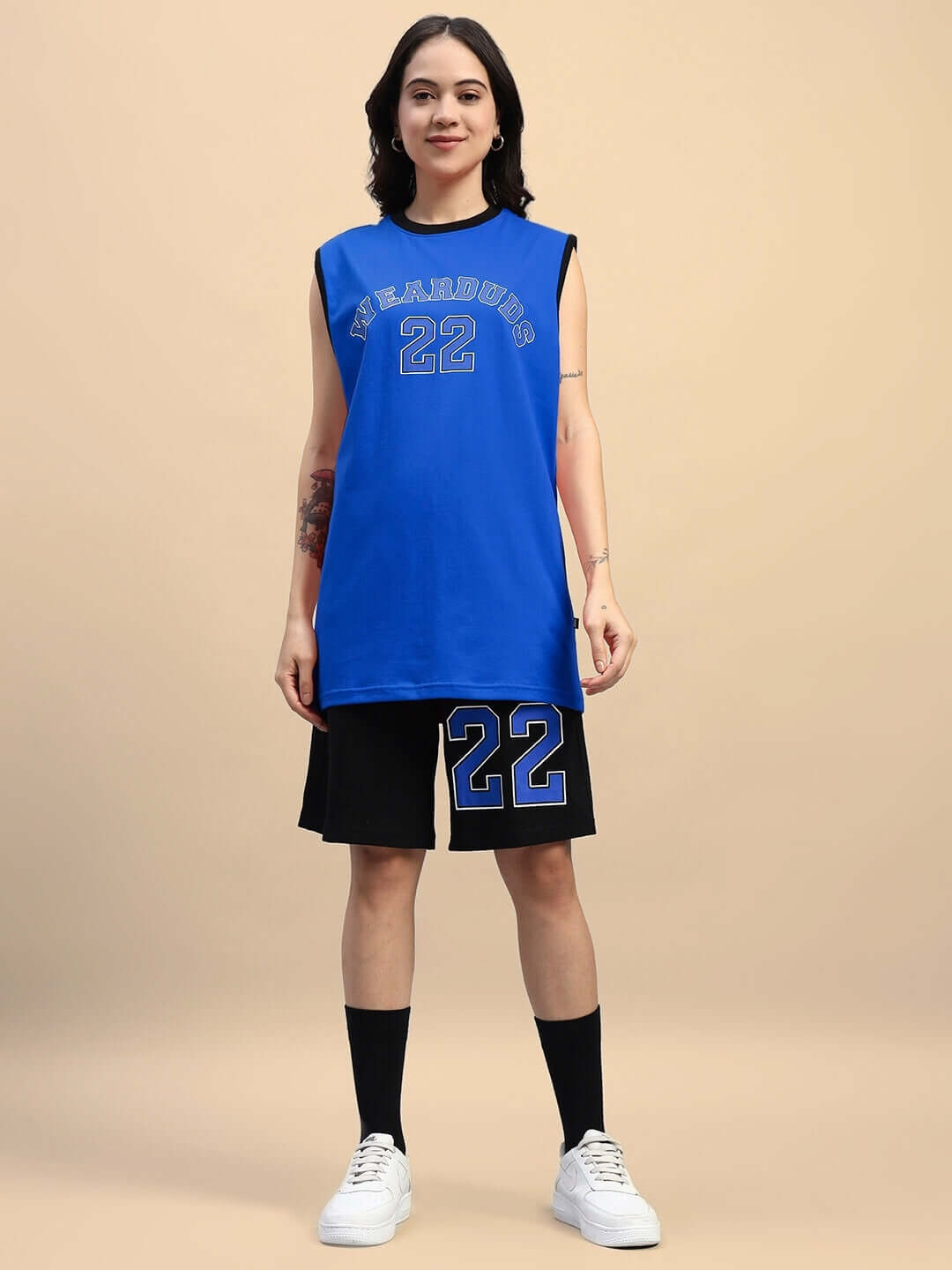 Woman wearing blue-black Amiga gym co-ord set, featuring a blue top with numeric design and black shorts, styled with white sneakers.