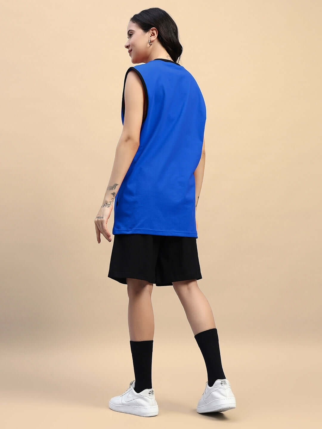 Woman wearing Amiga gym co-ord set in blue and black, featuring a sleeveless top and shorts, styled with sneakers and socks.