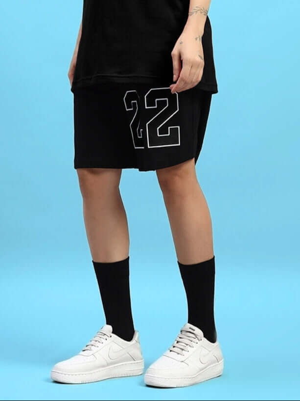 Woman wearing Women's Amiga Regular Fit Shorts in black, displaying custom fit option, paired with white sneakers and black socks.