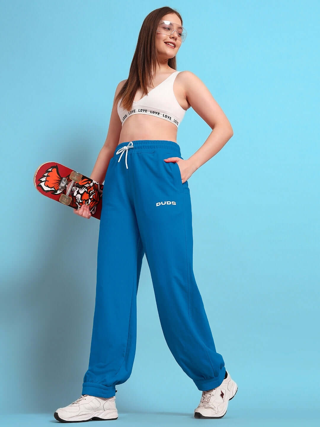 Woman wearing blue Austrian relaxed-fit joggers holding skateboard, stylish look by DUDS