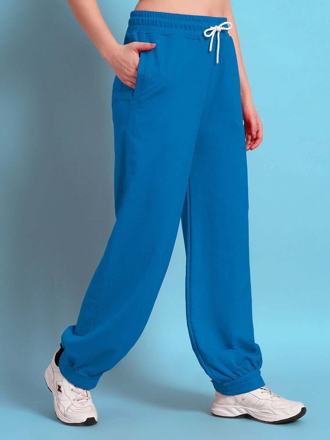 Model wearing Women's Austrian Relaxed-Fit Joggers in blue with elastic waistband and drawstring, paired with white sneakers.